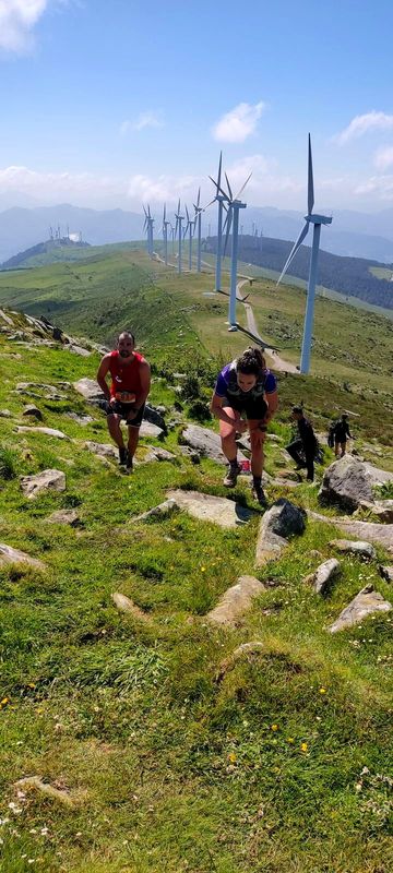 Corredores subiendo una cresta con los aerogeneradores del Oiz al fondo, dorsal 63 en primer plano