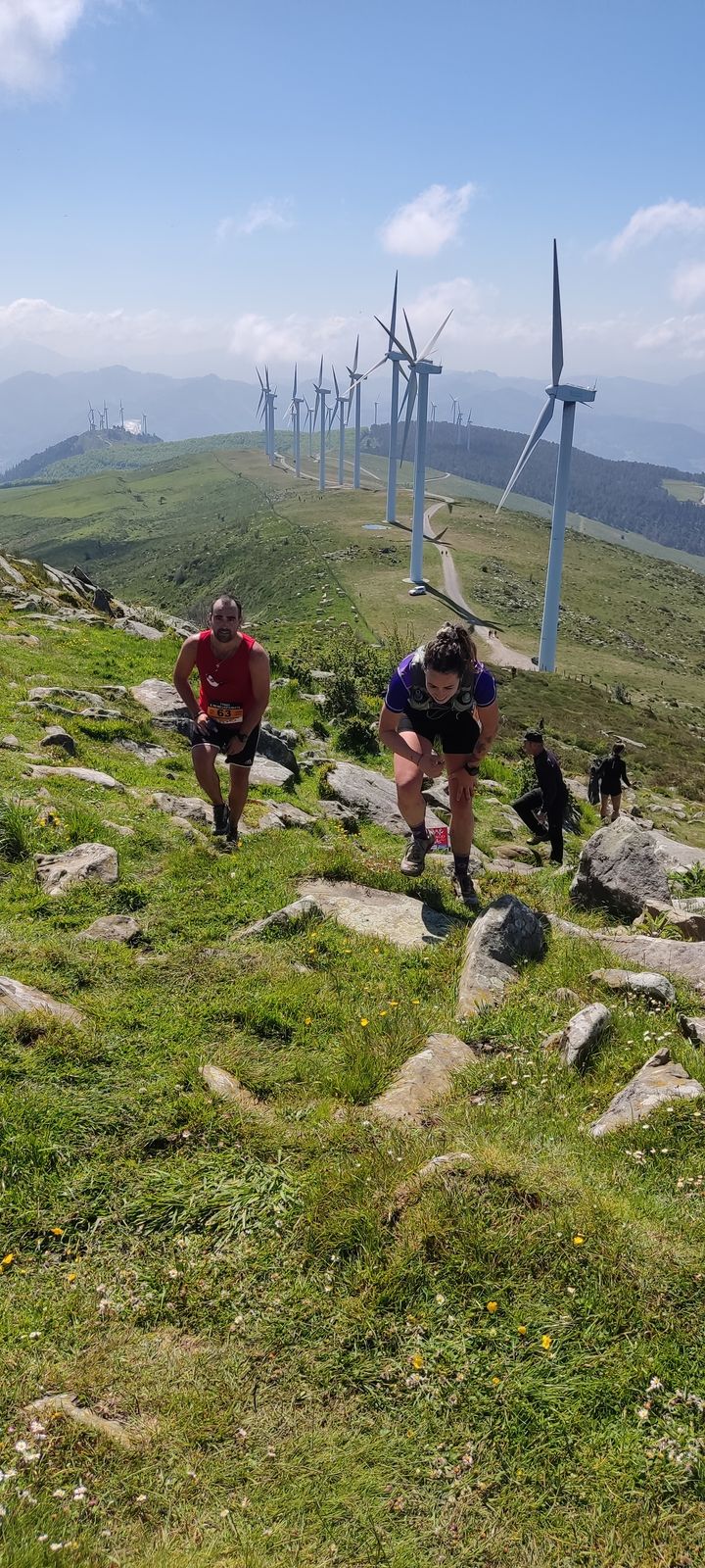 Corredores subiendo una cresta con los aerogeneradores del Oiz al fondo, dorsal 63 en primer plano