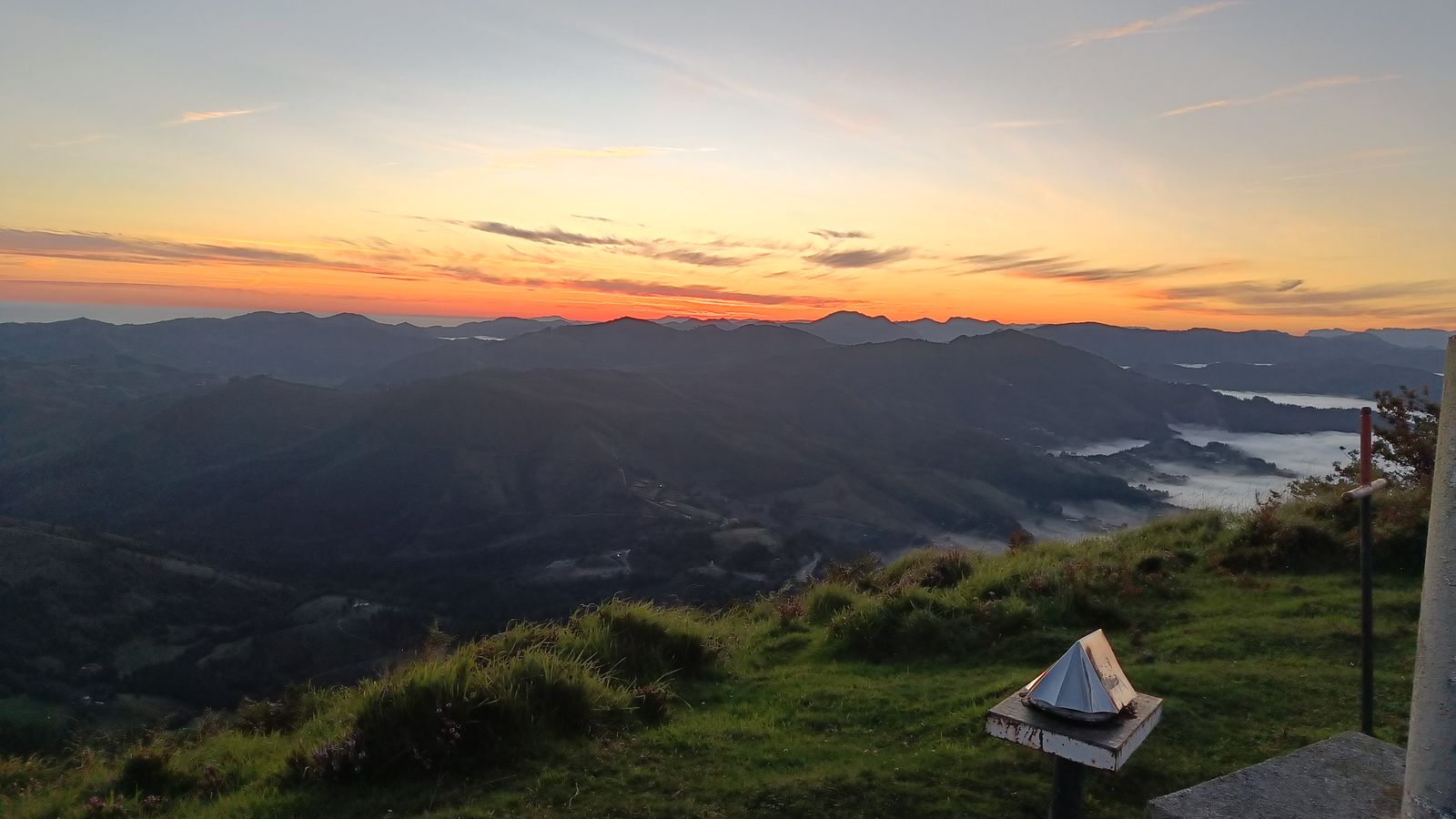 Amanecer desde una cima, con un v&eacute;rtice geod&eacute;sico en primer plano y valles entre niebla