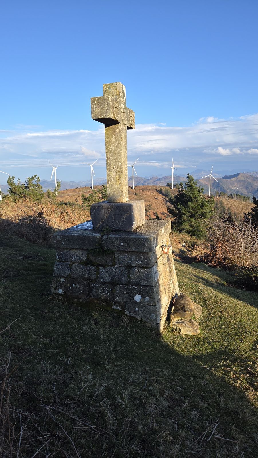 Cruz de piedra sobre un pedestal, con aerogeneradores al fondo