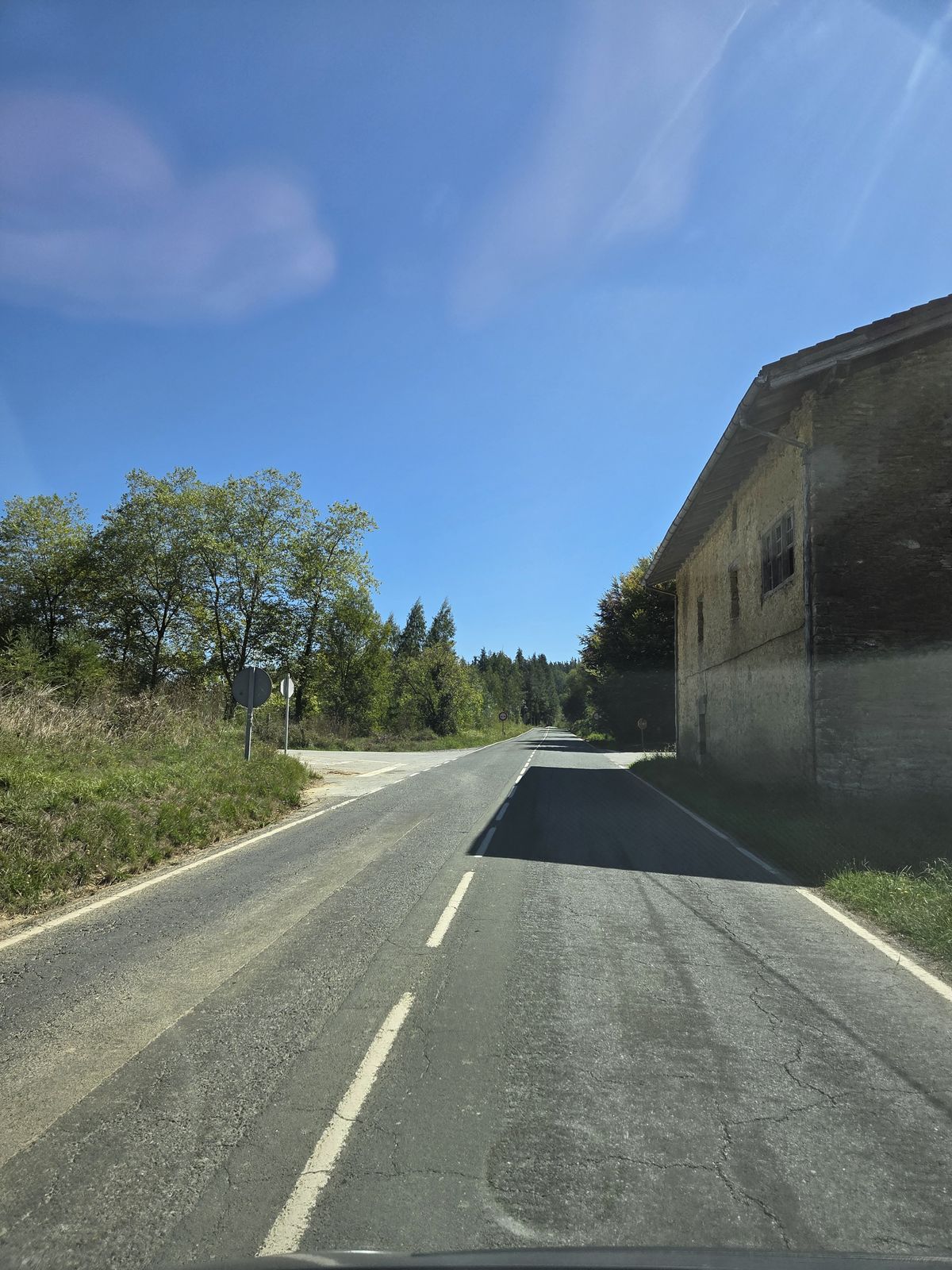 Edificio de piedra junto a la carretera, en una curva, entre arbolado