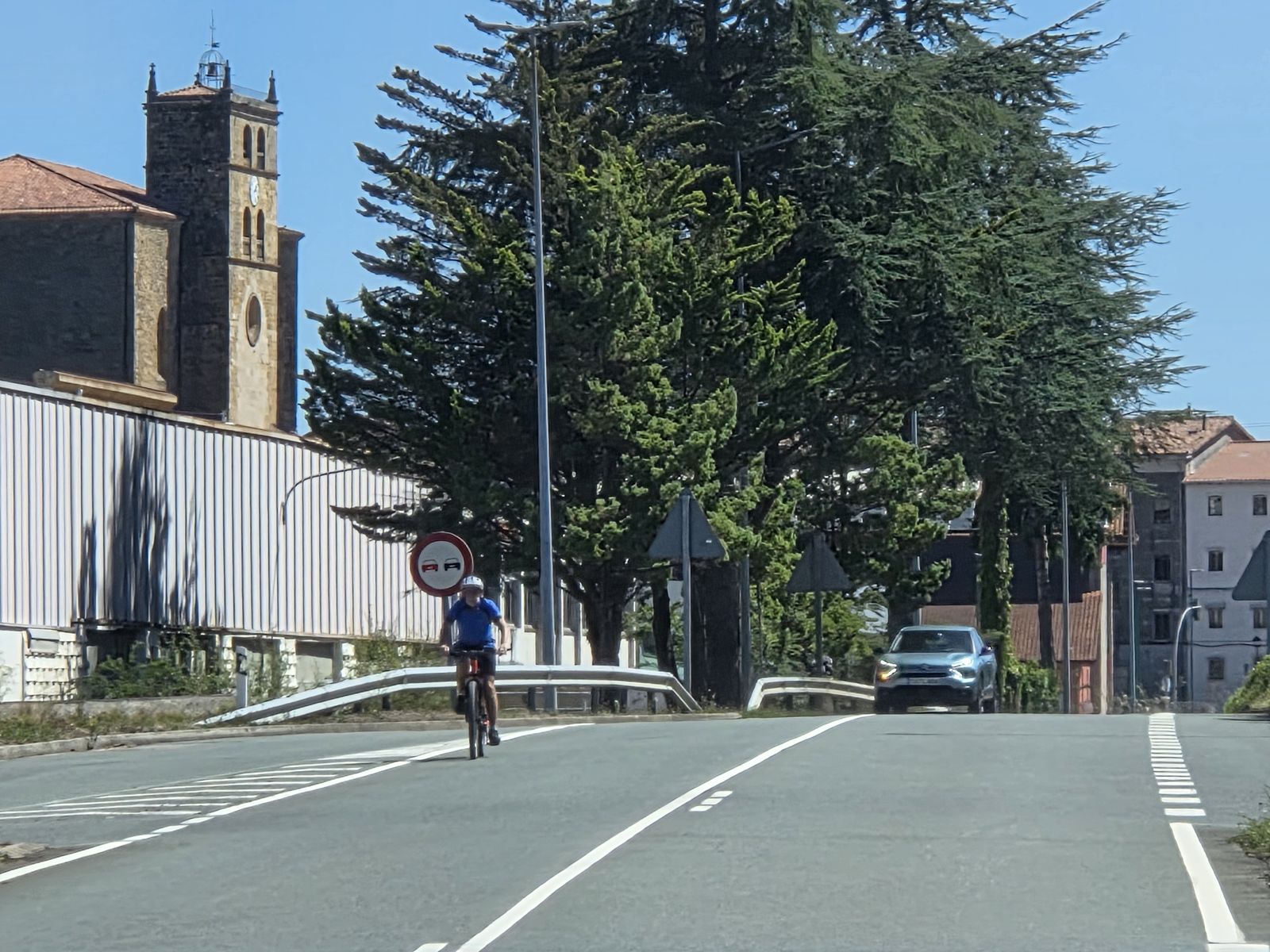 Ciclista subiendo por la carretera a la entrada del pueblo, con la torre de piedra de la iglesia a la izquierda