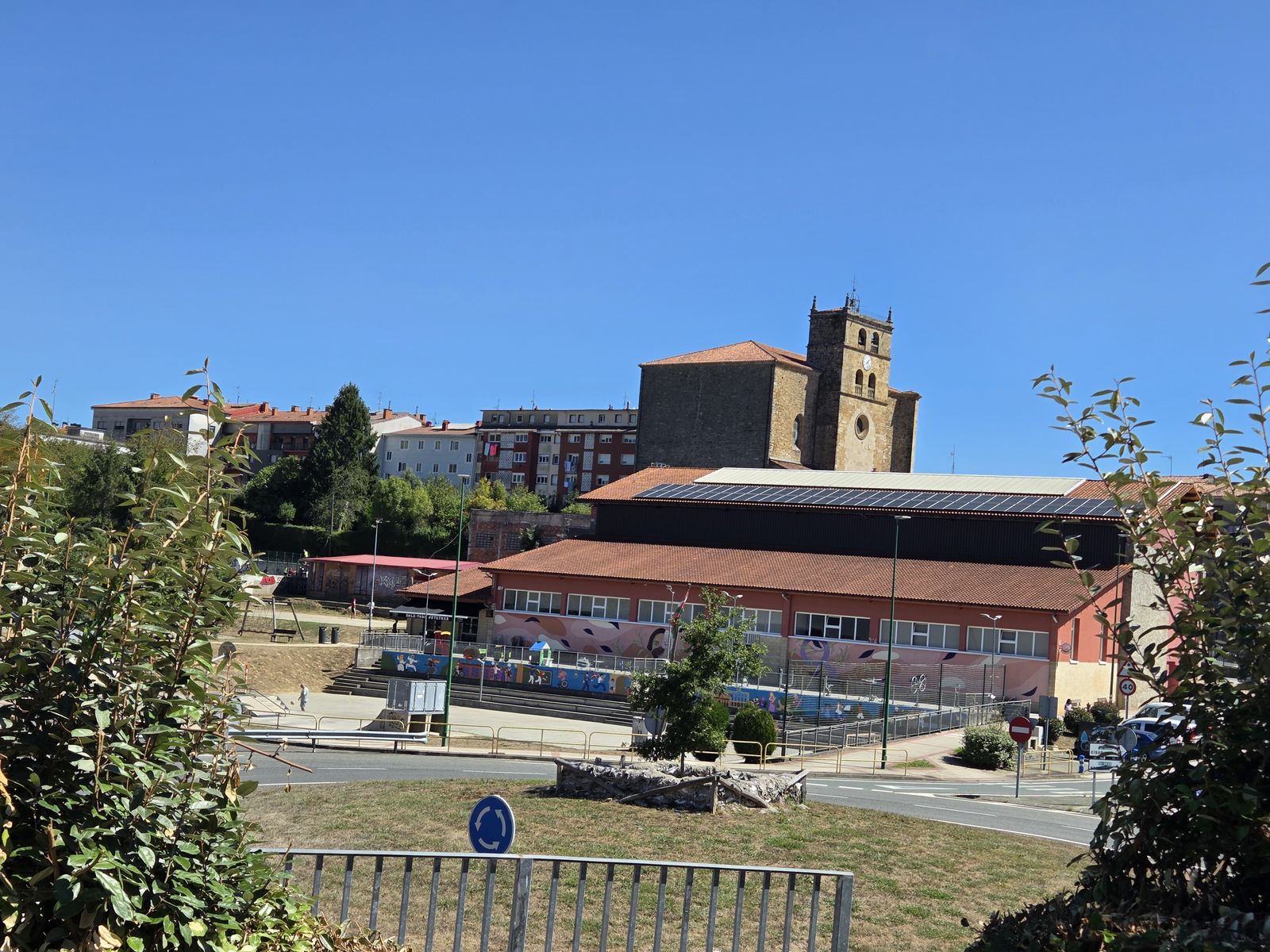 El pueblo visto desde la carretera, con la iglesia de piedra en lo alto y el front&oacute;n cubierto delante