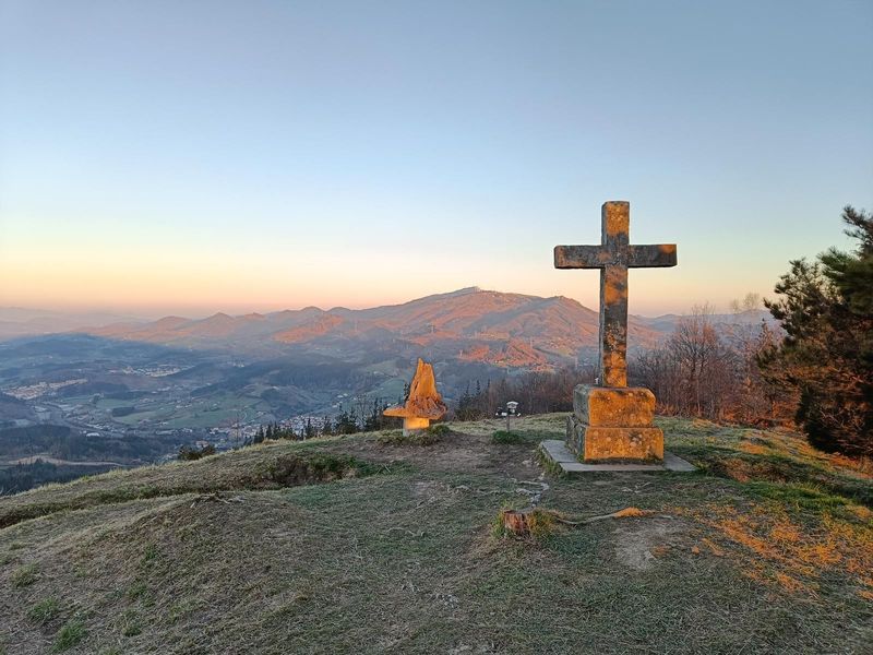La cruz de Santama&ntilde;azar al atardecer, con el valle y los montes del Duranguesado al fondo
