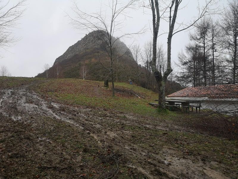 La pe&ntilde;a de Egoarbitza entre la niebla, con el refugio y la pista embarrada en primer plano