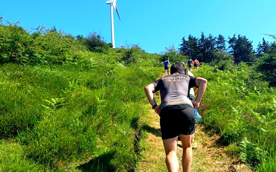 Corredor subiendo un sendero hacia un aerogenerador, con más corredores al fondo