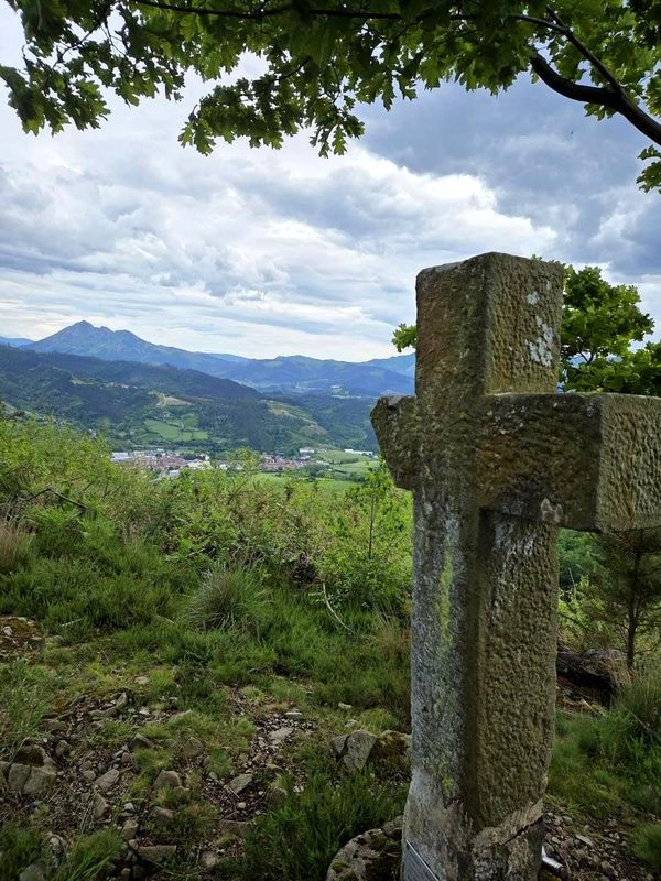 Una cruz de piedra con vistas al valle y a un monte al fondo, en verano