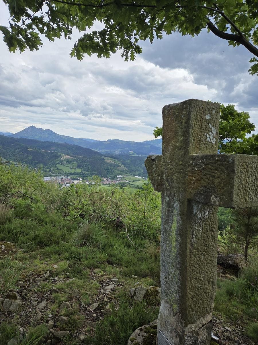 Una cruz de piedra con vistas al valle y a un monte al fondo, en verano