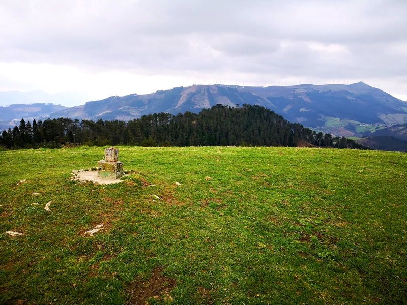 V&eacute;rtice geod&eacute;sico en la cima de Olamendi, con el parque e&oacute;lico del Oiz al fondo entre nubes