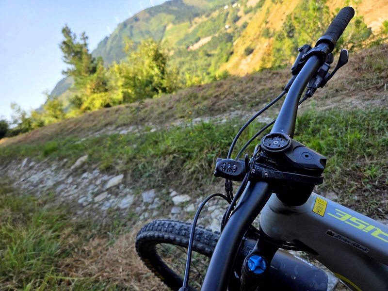 El manillar de la e-bike en primer plano sobre la pista, con la ladera del monte al fondo