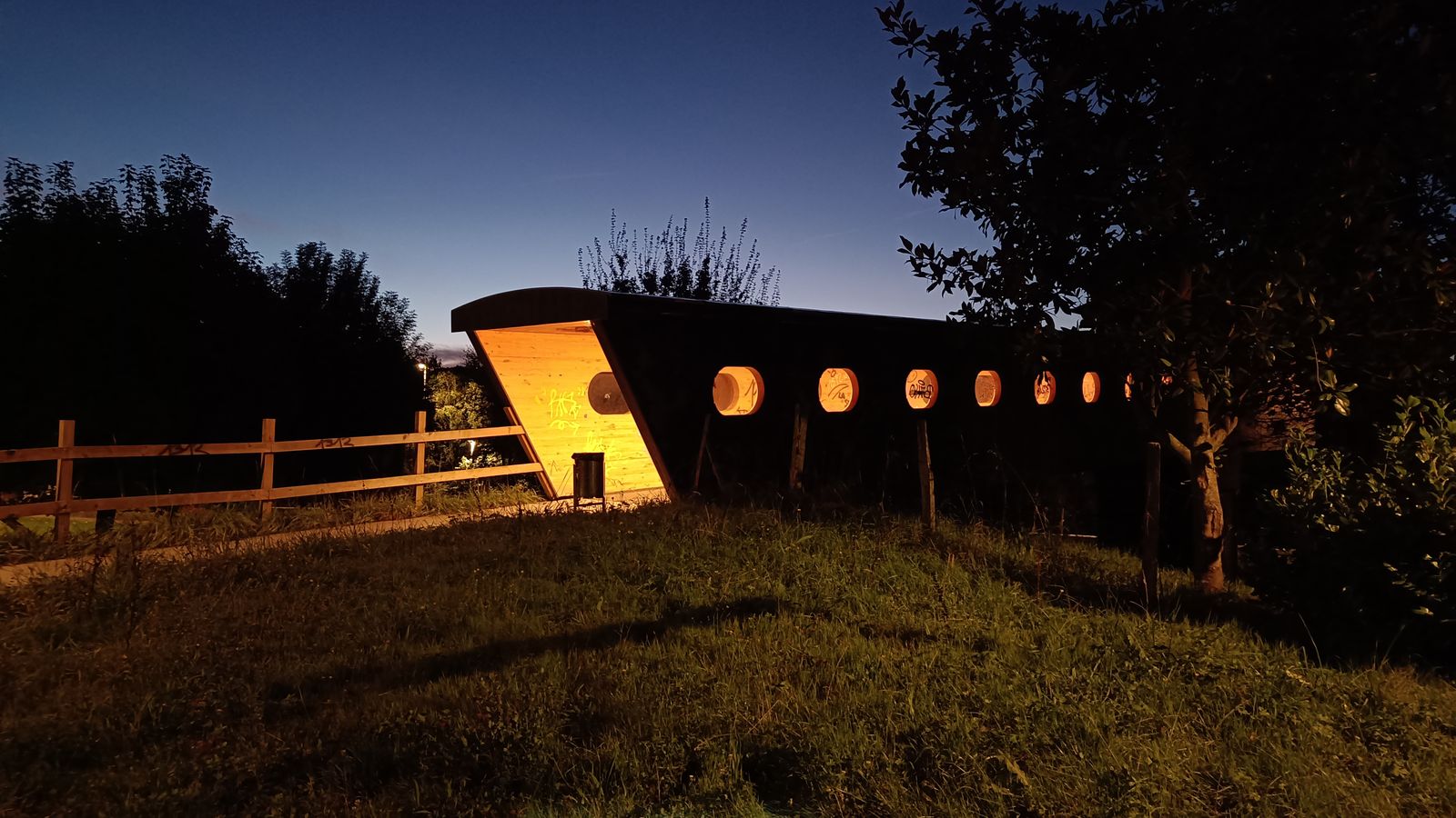 Refugio de madera iluminado de noche, con ventanas redondas