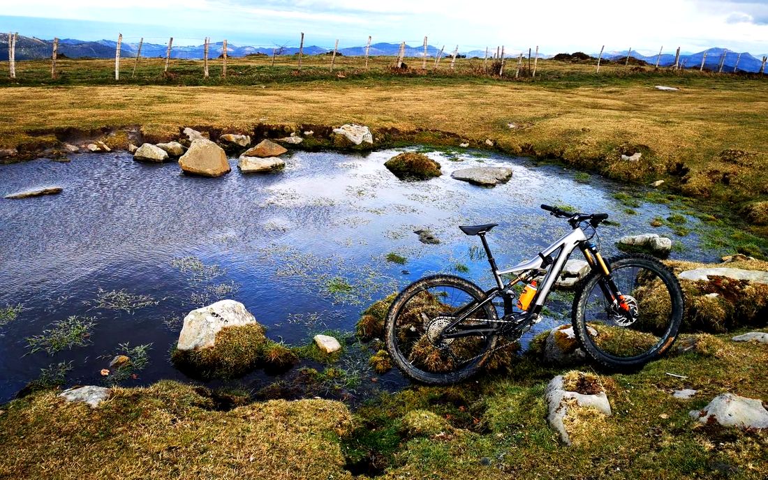 Bicicleta junto a una pequeña laguna de montaña, con una valla y vistas al fondo