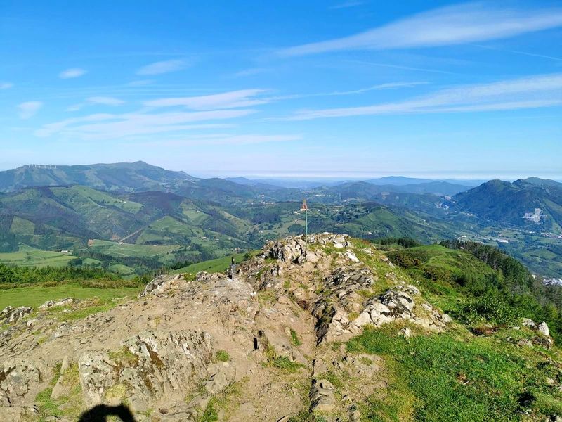 Se&ntilde;al de madera en una loma, con aerogeneradores y el mar al fondo