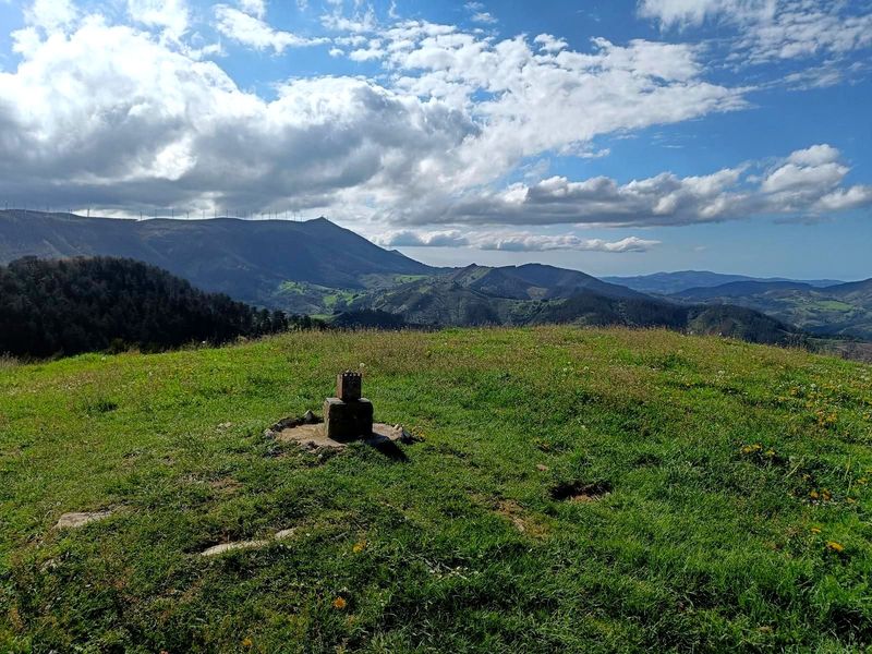Moj&oacute;n de piedra en un prado, con aerogeneradores en las monta&ntilde;as al fondo
