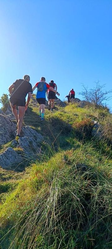 Corredores subiendo una cresta herbosa y rocosa bajo un cielo despejado
