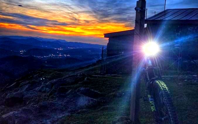 Bicicleta con el faro encendido junto a un poste de señalización, cerca de las antenas de la cumbre del Oiz al anochecer