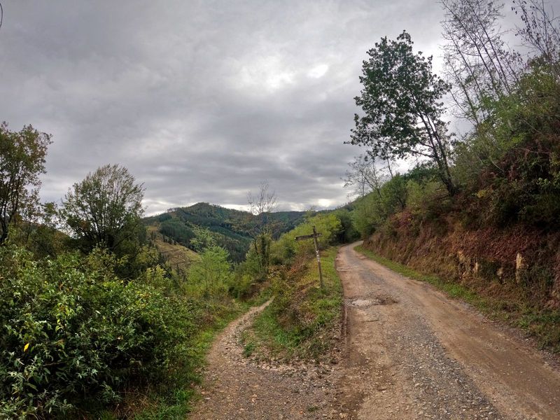 Cruce de pistas con un poste de madera, sobre las laderas de monte bajo un cielo nublado