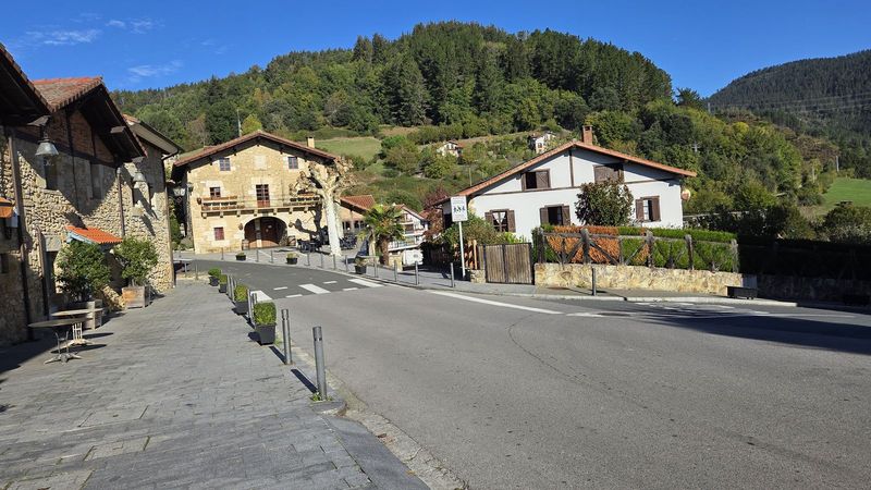 Plaza de un barrio con caser&iacute;os de piedra y la ladera boscosa detr&aacute;s