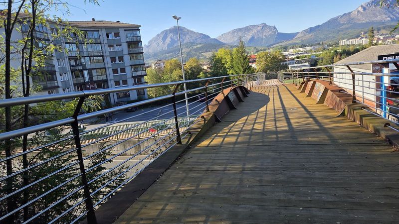 Pasarela de madera para peatones sobre la carretera, con las monta&ntilde;as al fondo