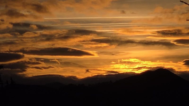 Nubes doradas al atardecer sobre las siluetas de los montes, con una antena en la cima a la derecha