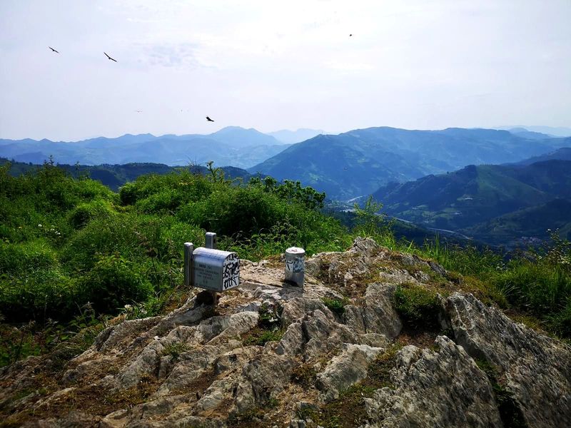 Se&ntilde;al de la cima de Urko (791 m), con aves volando y las monta&ntilde;as al fondo entre la calima