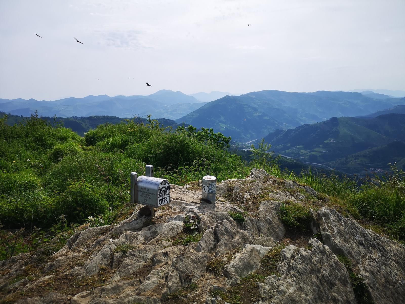 Se&ntilde;al de la cima de Urko (791 m), con aves volando y las monta&ntilde;as al fondo entre la calima
