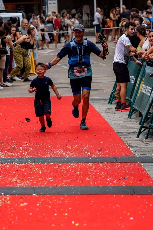 Llegada a meta por la alfombra roja entre confeti, de la mano de un ni&ntilde;o, con el p&uacute;blico animando a los lados
