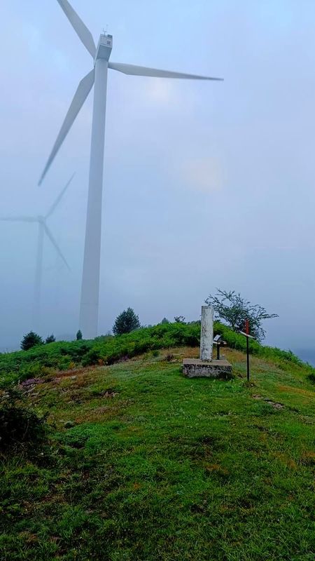 Eolikoa lainoartean belarrezko muino baten gainean, harrizko monolito bat eta metalezko gurutze bat lehen planoan
