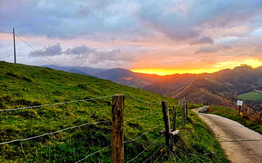 Atardecer sobre una pista rural cercada, con montes iluminados de naranja al fondo