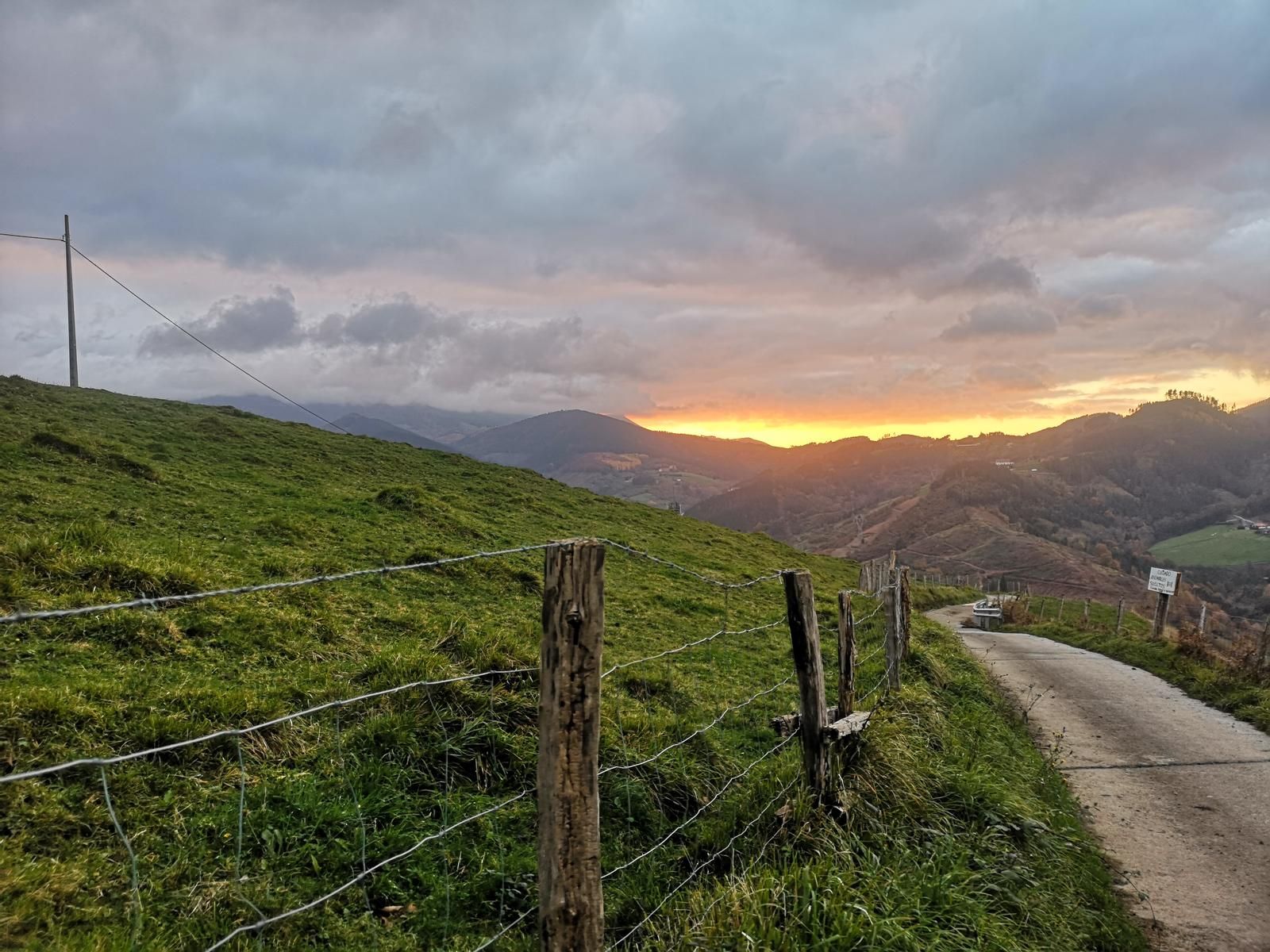 Atardecer sobre una pista rural cercada, con montes iluminados de naranja al fondo