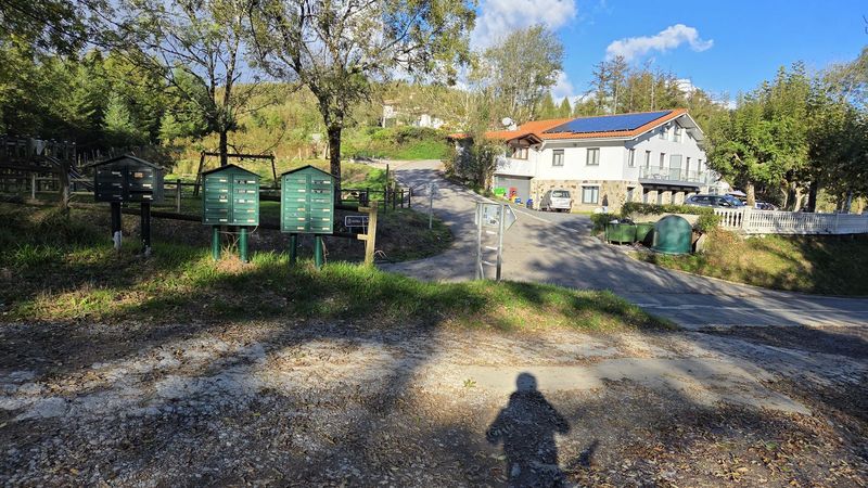 Errepidera irteera postontzi berde batzuen ondoan, teilatu gorriko eta eguzki-plakadun eraikin bat beste aldean