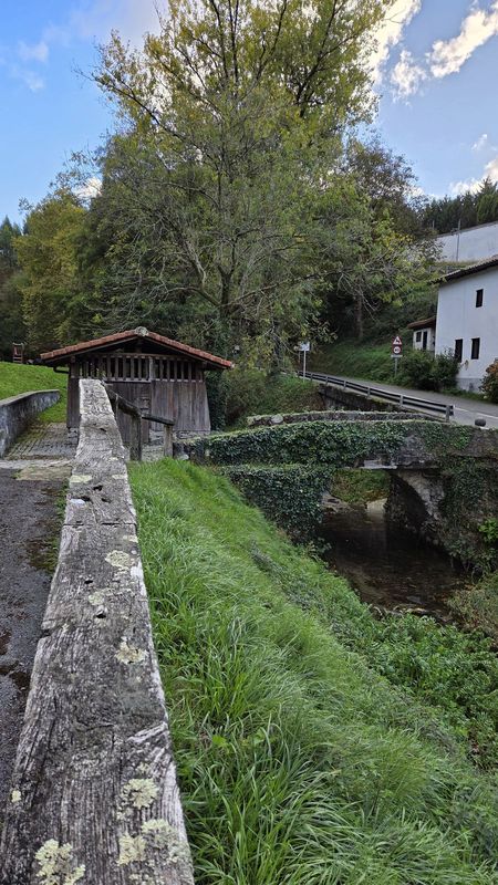 Huntzez estalitako harrizko zubia ibaiaren gainean, teila-teilatuko egurrezko etxola baten ondoan