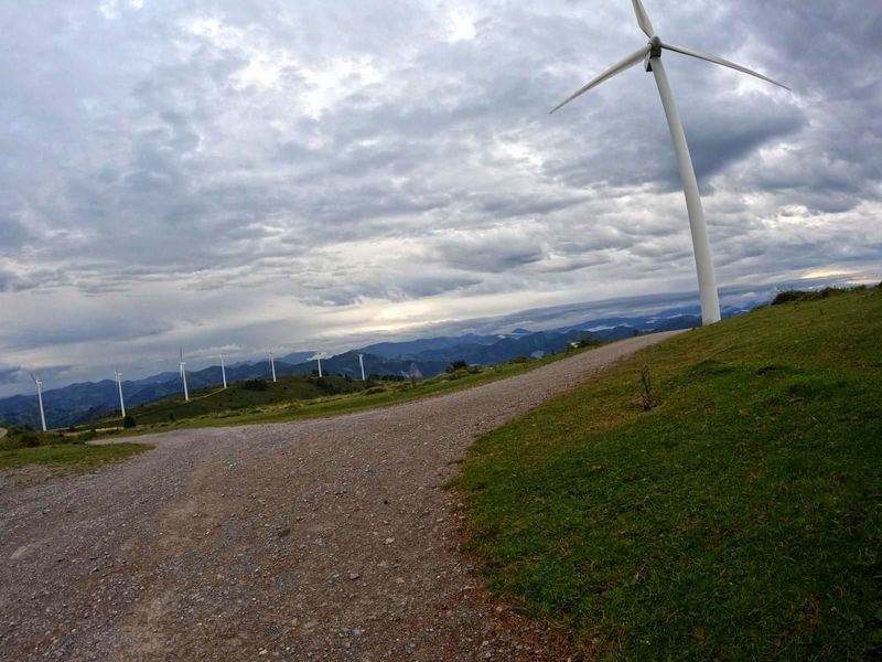 Aerosorgailua legarrezko pista baten ondoan, parke eolikoa atzealdean zeru hodeitsu baten azpian