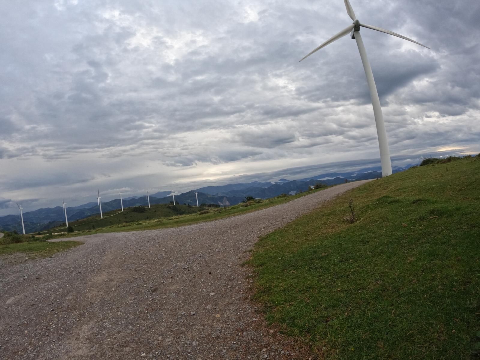 Aerosorgailua legarrezko pista baten ondoan, parke eolikoa atzealdean zeru hodeitsu baten azpian