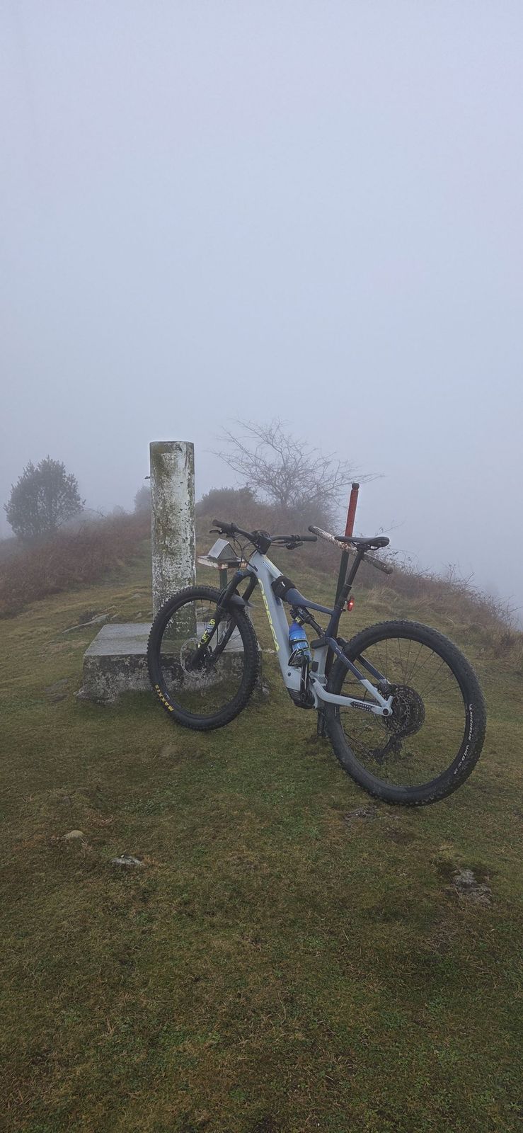 Bicicleta de montaña apoyada en un mojón de piedra, con niebla