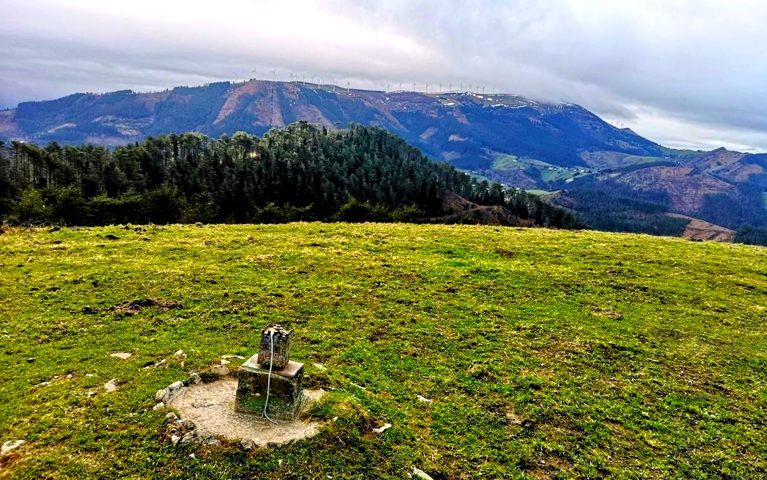 Mojón en la cima del Mendibil, con el parque eólico y el pueblo al fondo