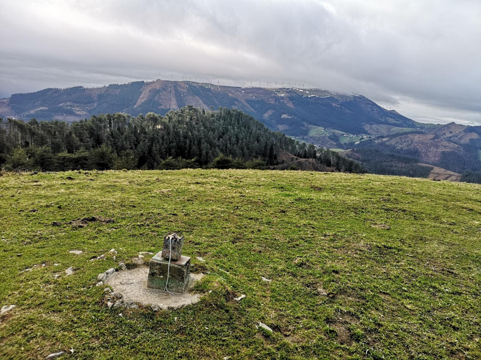 Mendibilgo gailurreko mugarria, parke eolikoa eta herria atzealdean
