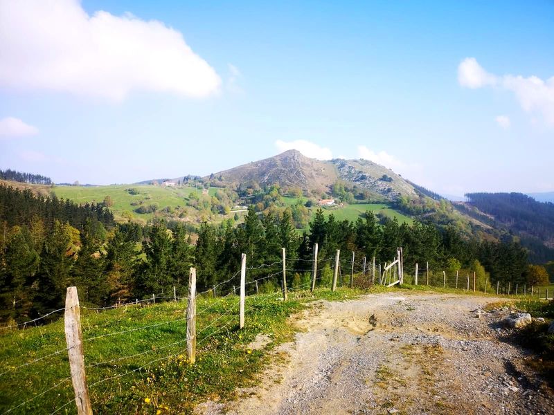 Pico rocoso al fondo, visto desde un camino de tierra junto a una alambrada, con caser&iacute;os dispersos en la ladera
