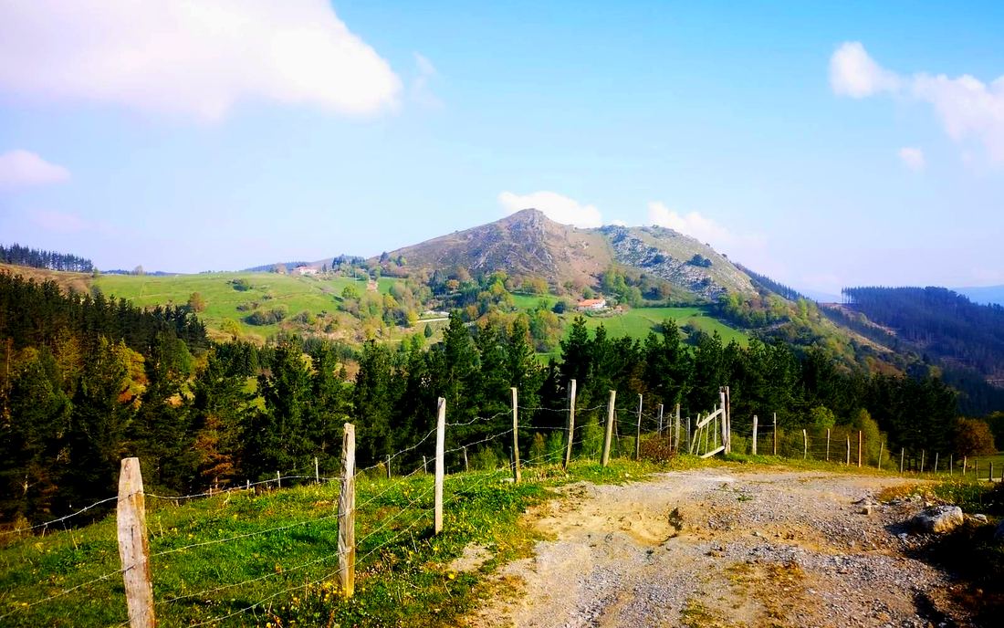 Pico rocoso al fondo, visto desde un camino de tierra junto a una alambrada, con caseríos dispersos en la ladera