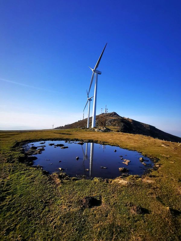 Aerogeneradores del Oiz reflejados en un charco de la cumbre, con las antenas al fondo