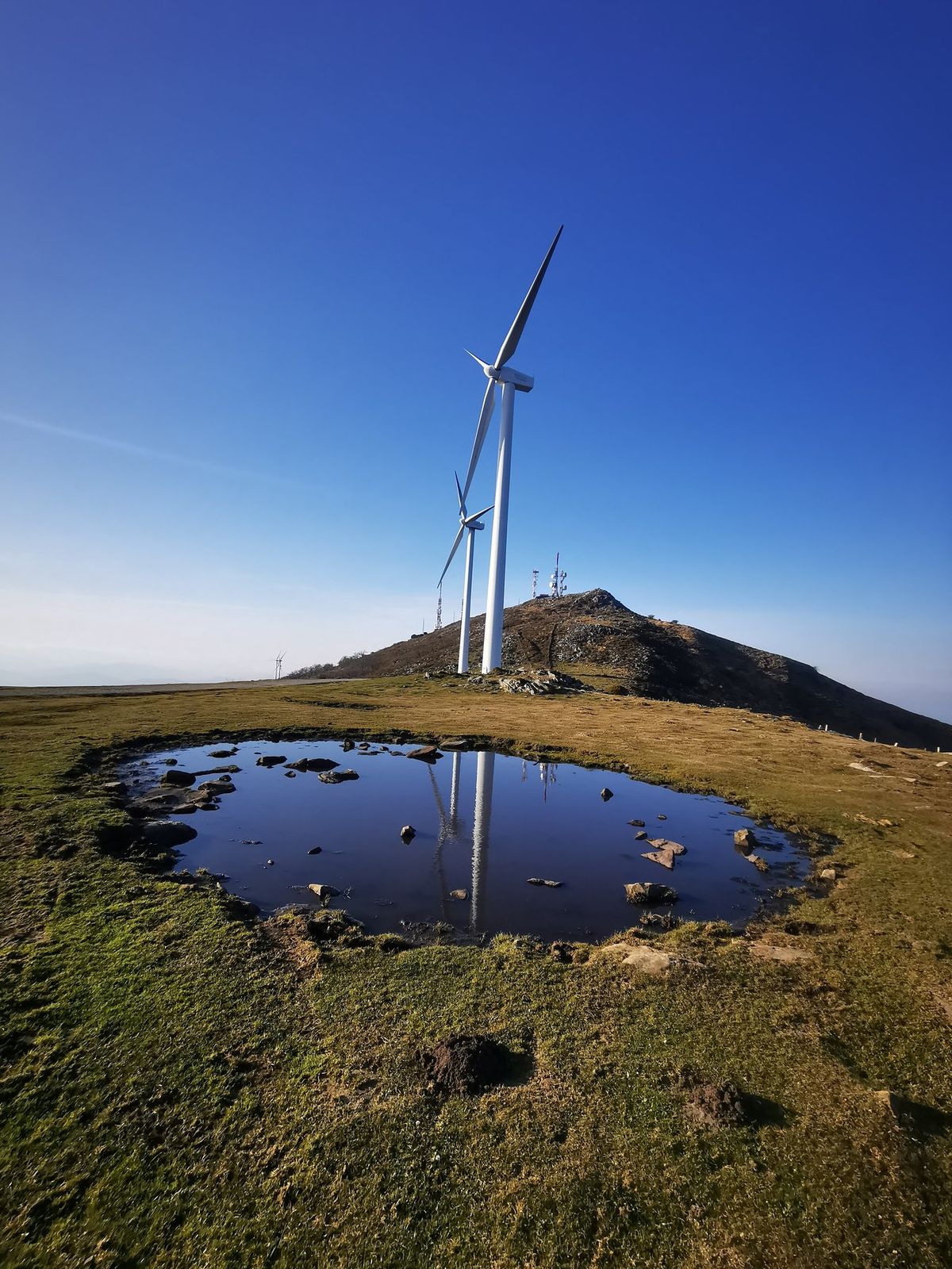 Aerogeneradores del Oiz reflejados en un charco de la cumbre, con las antenas al fondo