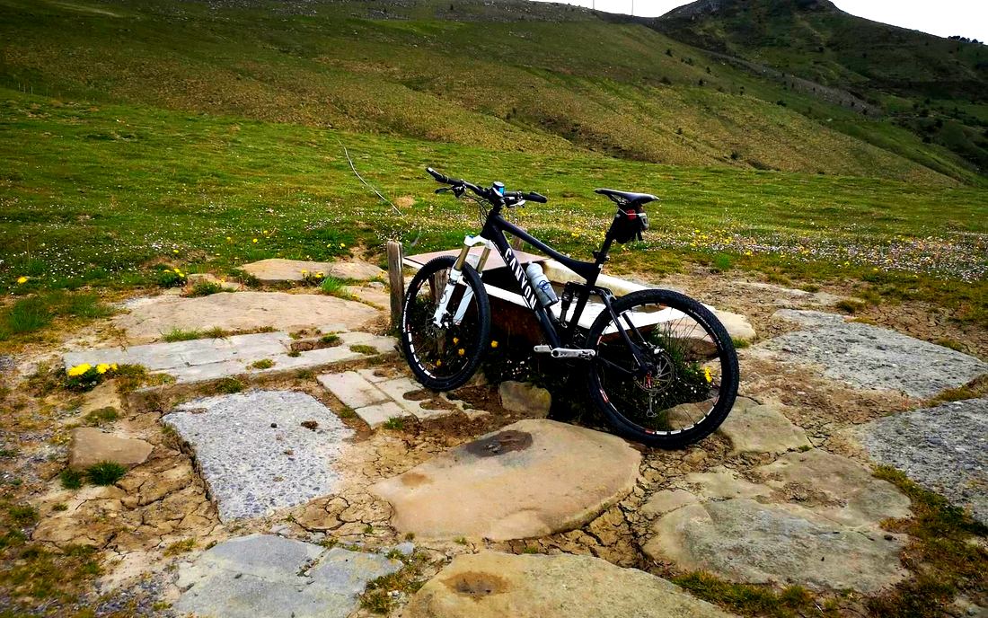 Bicicleta de montaña apoyada en un abrevadero de piedra en el cordal, con los aerogeneradores y la cima del Oiz al fondo