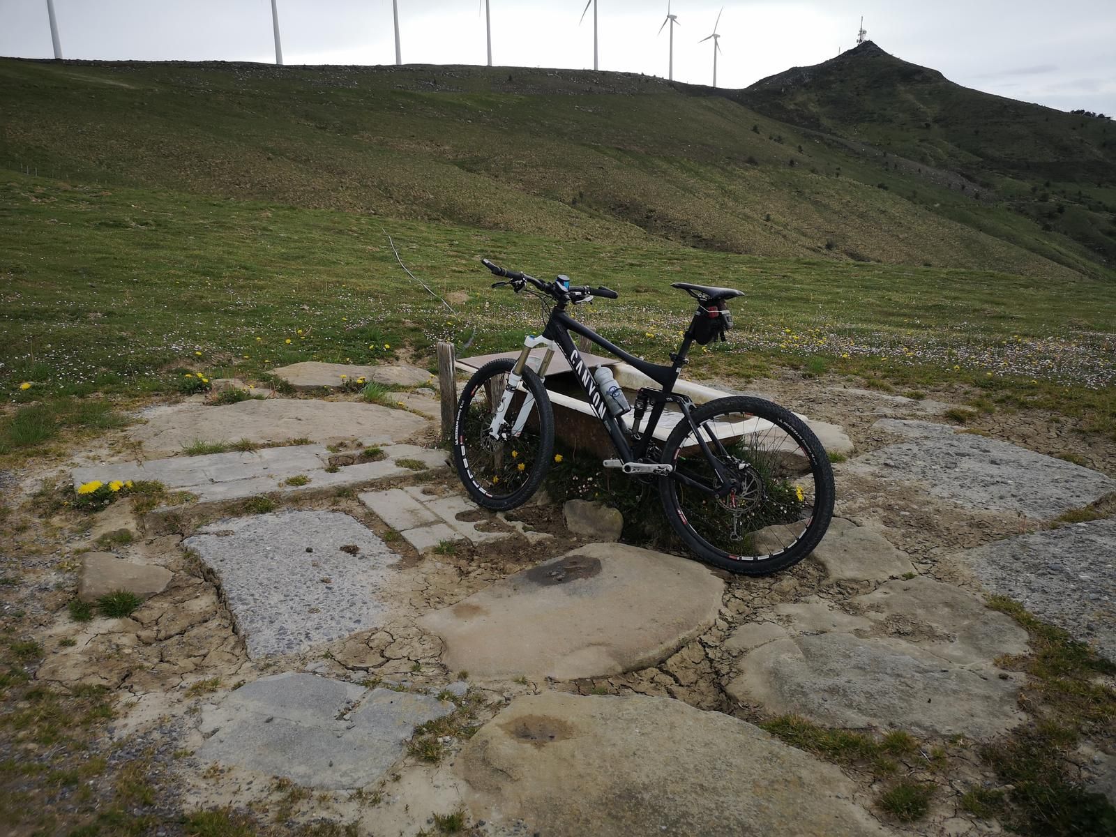 Bicicleta de monta&ntilde;a apoyada en un abrevadero de piedra en el cordal, con los aerogeneradores y la cima del Oiz al fondo