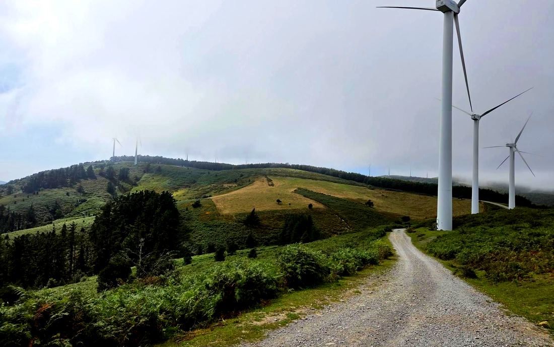 Pista junto a los aerogeneradores del parque eólico, con niebla cubriendo la cresta
