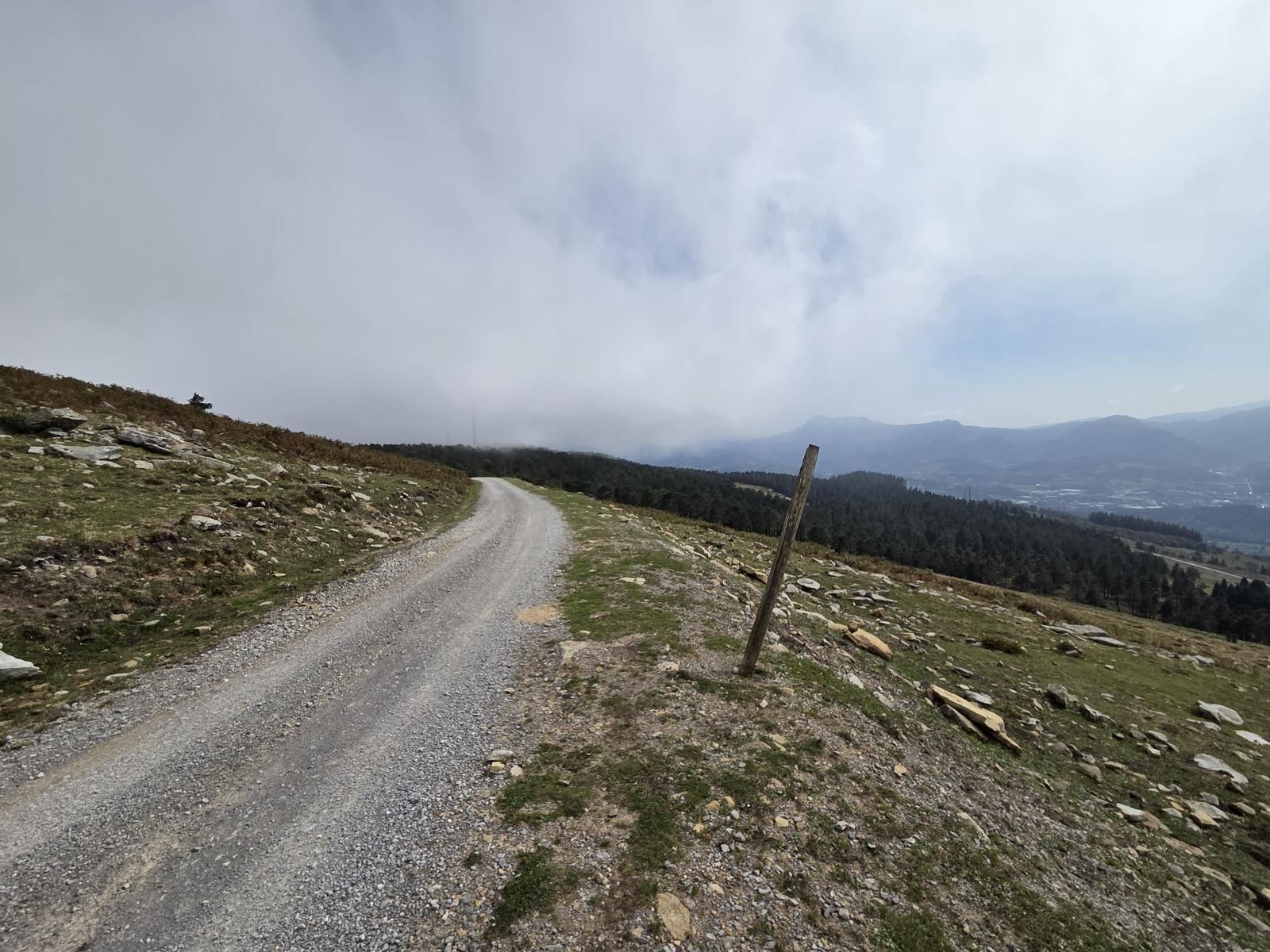 Pista de tierra con un poste de madera, y el valle del Duranguesado al fondo