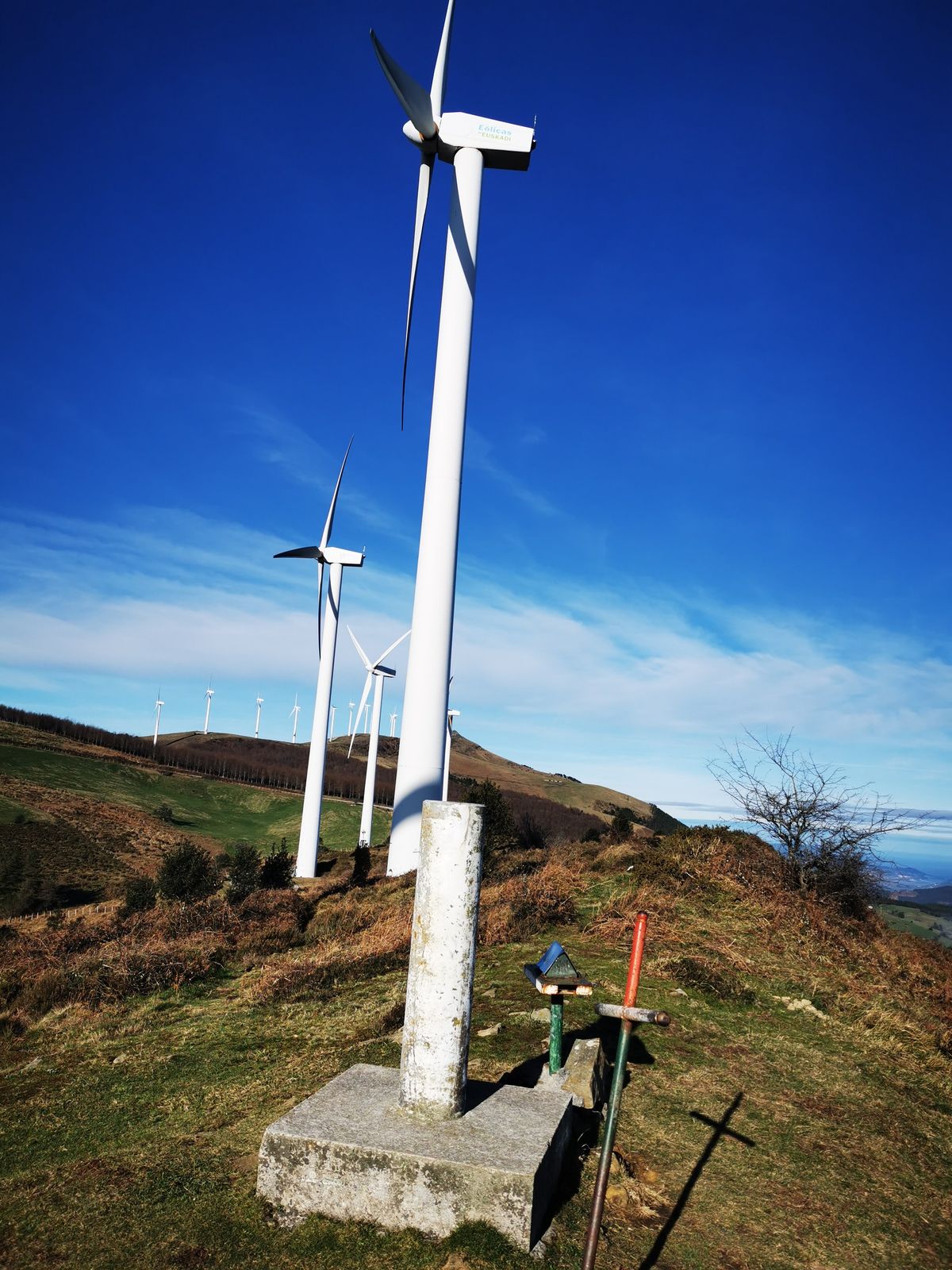 Bertize geodesikoa eta gurutzea Oizko gailurrean, parke eolikoko aerosorgailuak atzealdean