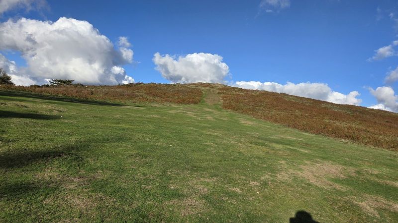 Campa herbosa subiendo hacia la cumbre de Kalamua, con nubes blancas sobre el cordal