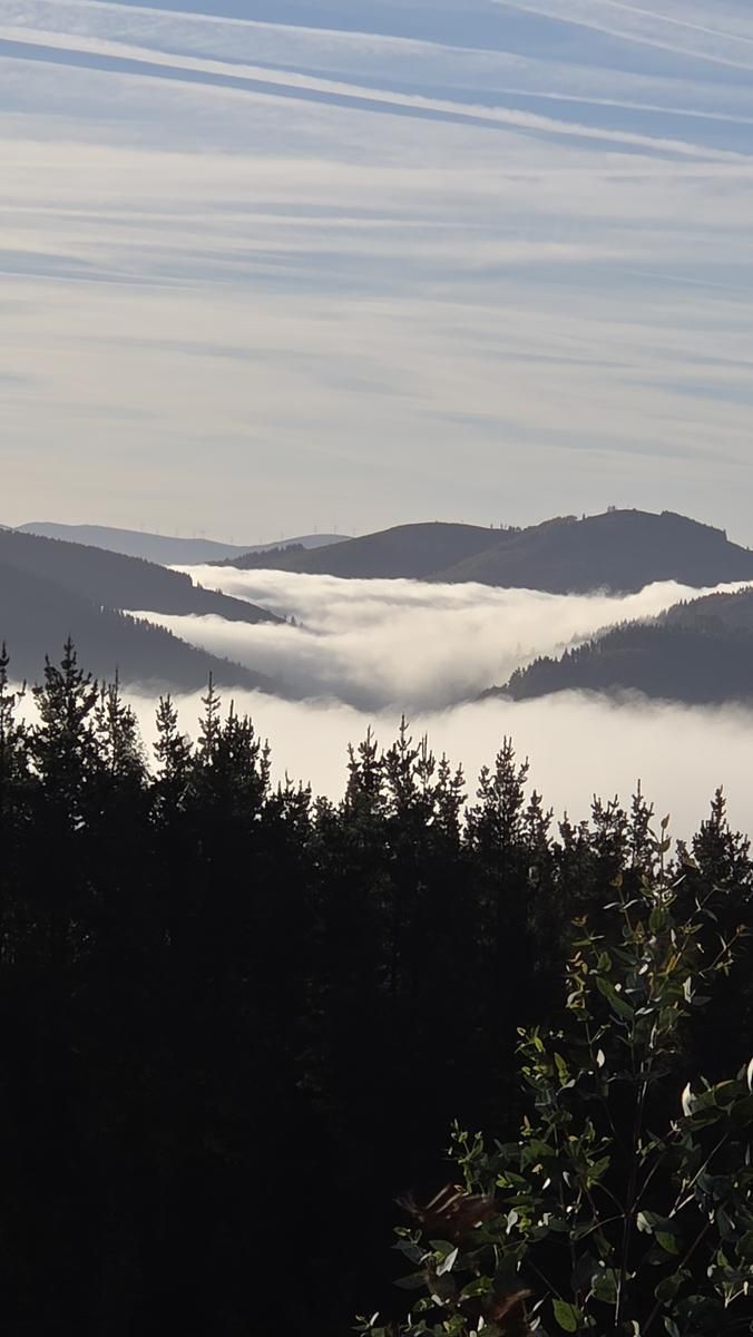 Niebla llenando el valle entre las crestas, con estelas de aviones en el cielo