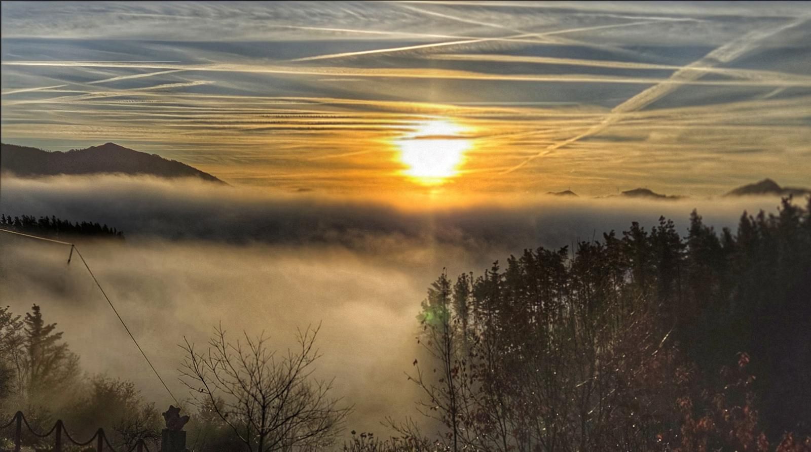 Amanecer entre estelas de aviones, con nubes bajas cubriendo el valle