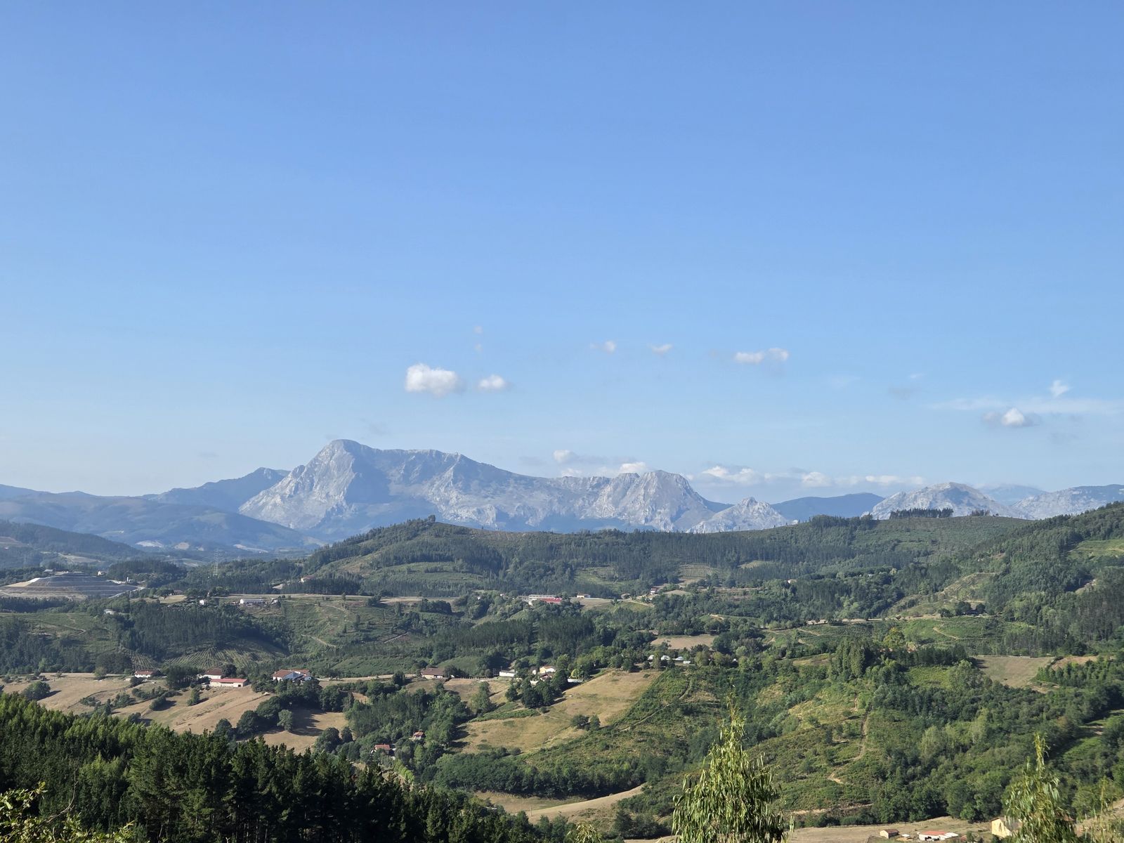 Vista panorámica de las montañas del entorno bajo un cielo despejado, con caseríos y prados en el valle en primer plano